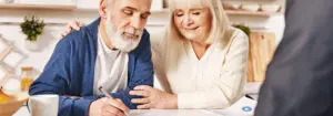 Senior couple smiling and signing paperwork