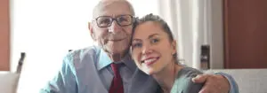 Elderly man smiling sitting with his arm around his granddaughter