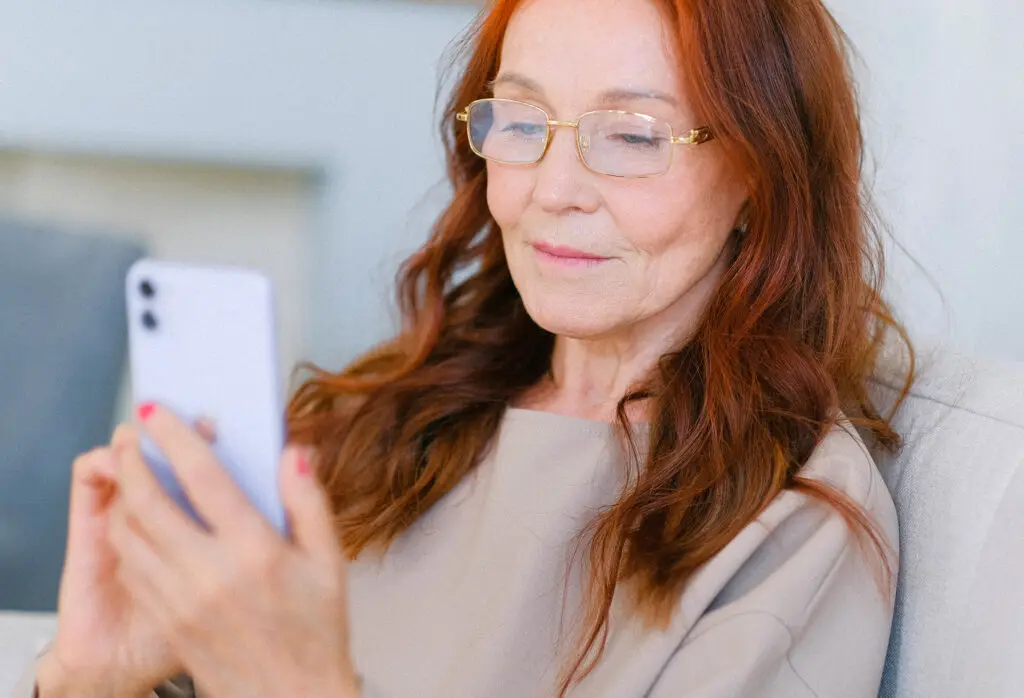 Elderly woman with red hair and eyeglasses making video call on her phone