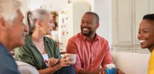 Senior and mature couples in conversation at home. Cheerful multiethnic group of people enjoying a cup of tea while talking to each other. Group of senior people socializing over coffee.