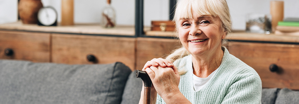 Senior woman holding cane and sitting on couch