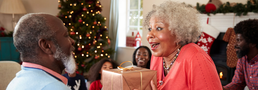 Senior woman smiling at man giving present by Christmas tree