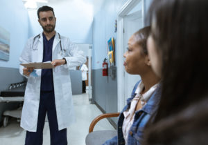 doctor holding clipboard approaching people sitting on bench in hospital