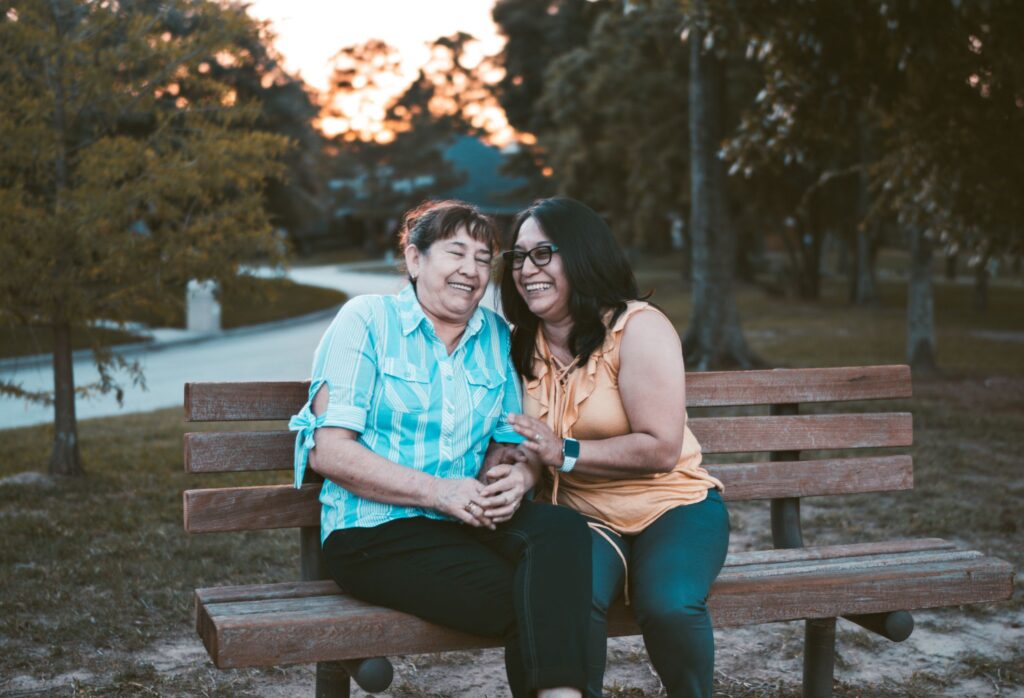 senior mother and adult daughter laughing on bench