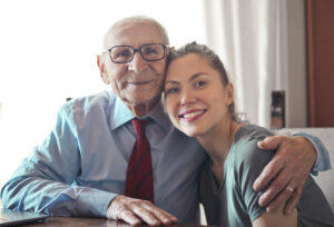 Elderly man smiling sitting with his arm around his granddaughter