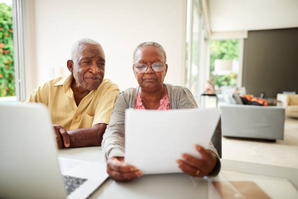 Shot of a african senior couple reading document with laptop at home | McGregor PACE