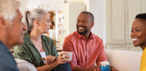 Senior and mature couples in conversation at home. Cheerful multiethnic group of people enjoying a cup of tea while talking to each other. Group of senior people socializing over coffee.